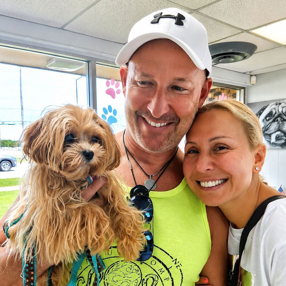 couple smiling and posing while holding a small dog